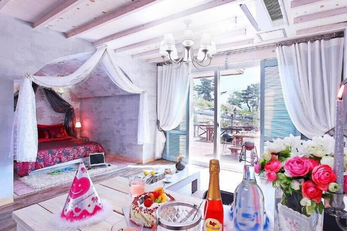 A bedroom with a canopy bed, a dining area with a table set for a meal, and a balcony with a view.