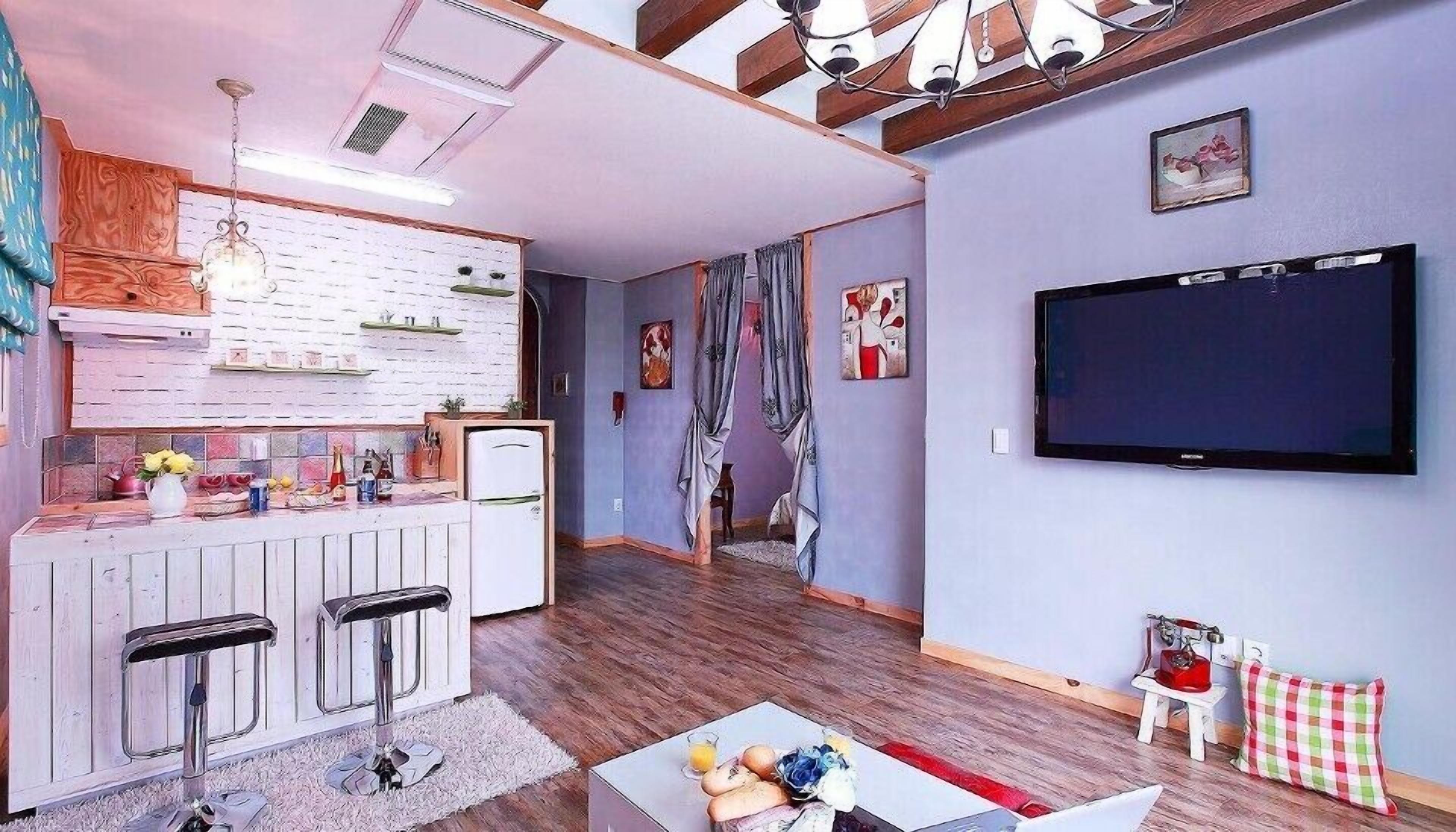 A modern living room with a TV, a kitchen area with a fridge, and a dining table with chairs.