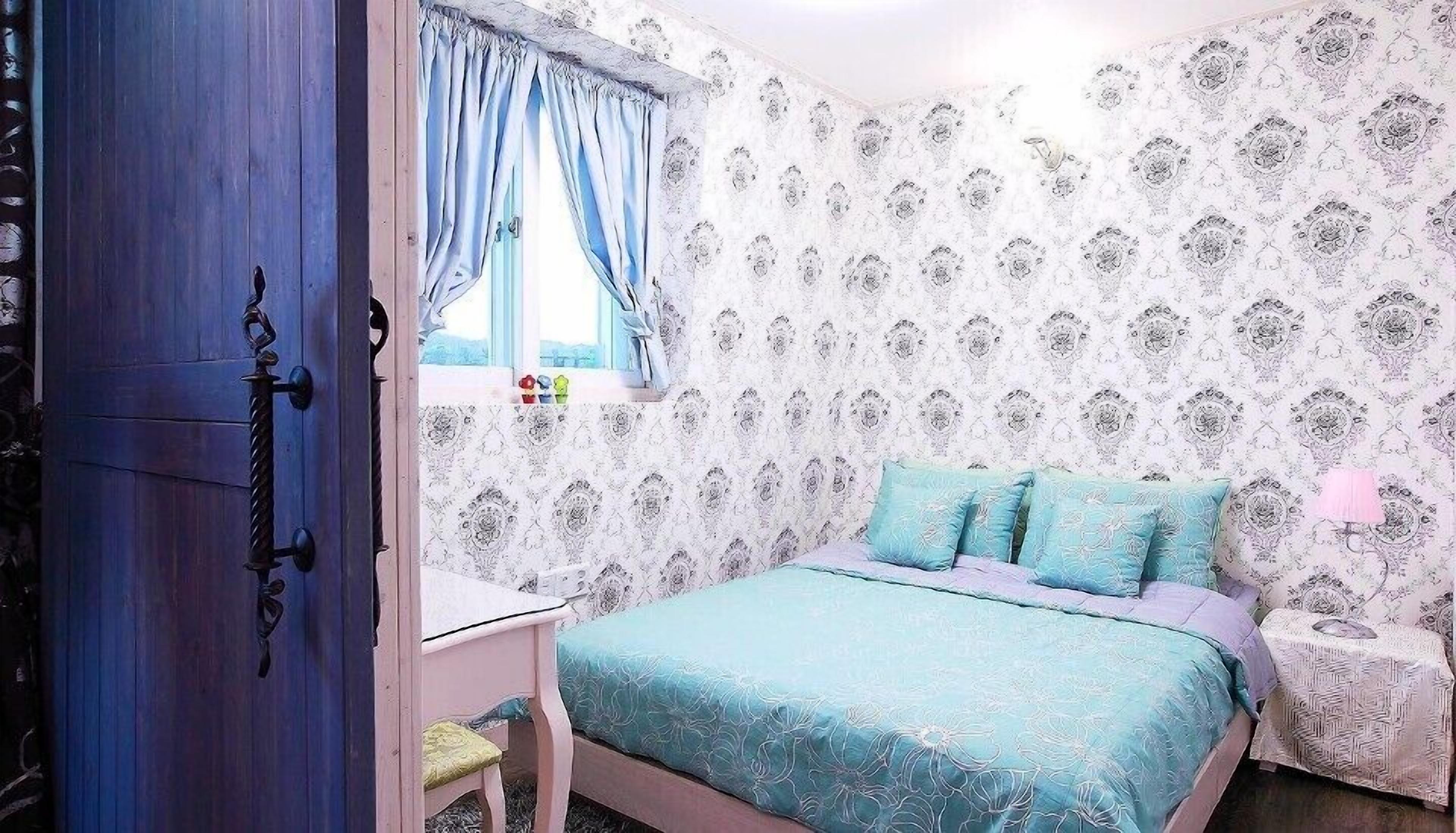 Een slaapkamer met een bed, nachtkastje, lamp en een raam met gordijnen.