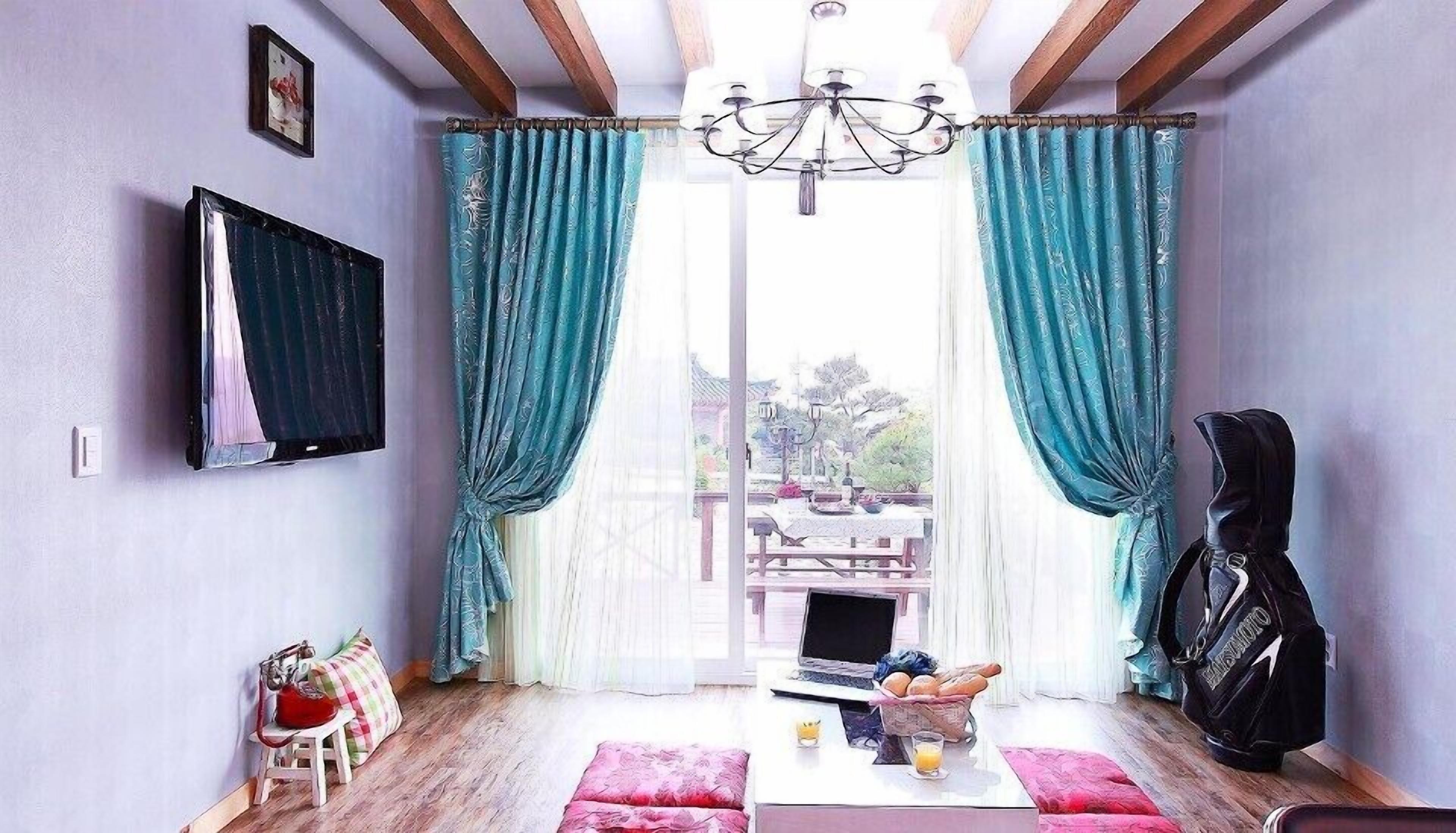 Una habitación con una televisión montada en la pared, un ordenador portátil sobre una mesa y una silla con un bolso.