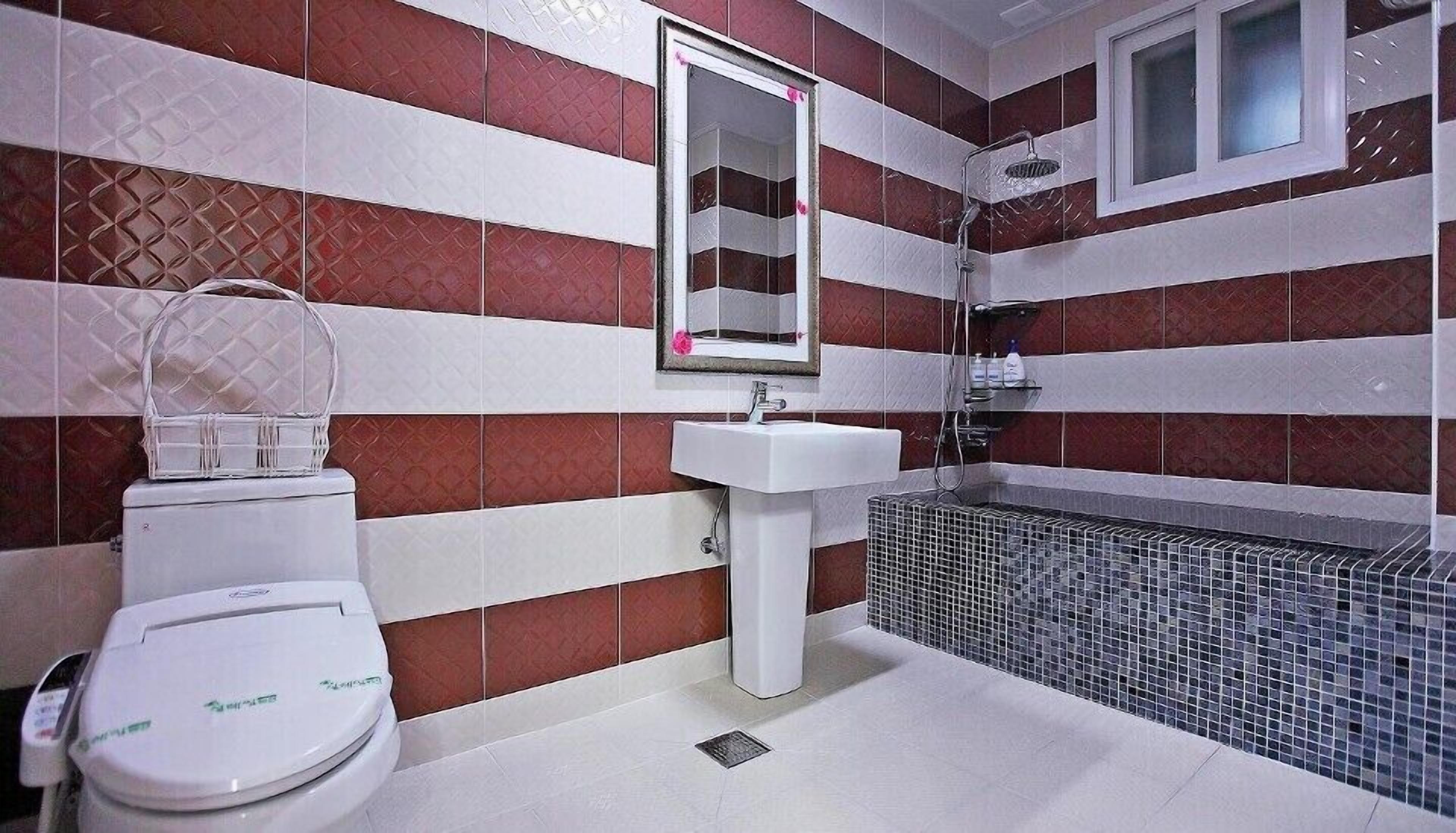 A bathroom with striped red and white tiles, a white sink, a toilet, and a shower area.