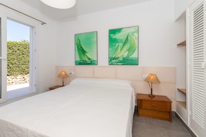 A bedroom with a bed, two wall-mounted lamps, a nightstand, a wooden drawer, and two sailboat paintings on the wall.