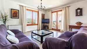 A living room with a sofa, a glass coffee table, a television, and a view of the outdoors. - Rural Villa with pool and a view – Villa Rote (Campanet)