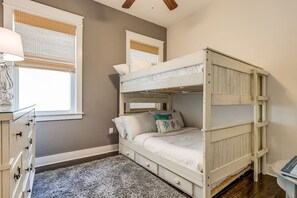 Uma cama beliche com acabamento branco, uma cômoda com gavetas e uma janela com persianas.