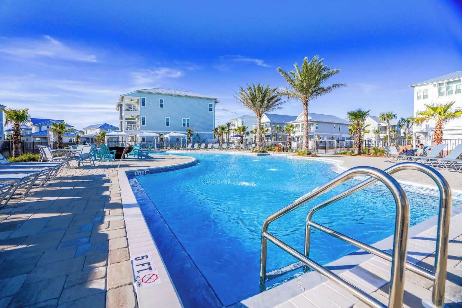 Une piscine dont la profondeur est indiquée à 1,5 mètre, entourée de chaises longues et de palmiers, avec des bâtiments visibles à l’arrière-plan.