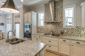 A kitchen with a granite countertop, stainless steel appliances, white cabinetry, and a patterned backsplash.