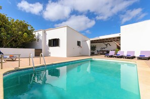A swimming pool with lounge chairs, a small building with a door, and a pergola with chairs.