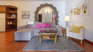Ein Wohnzimmer mit einer Couch, einem Couchtisch, einem weißen Sessel, einem Holzschrank und einer dekorativen Zierbogen.