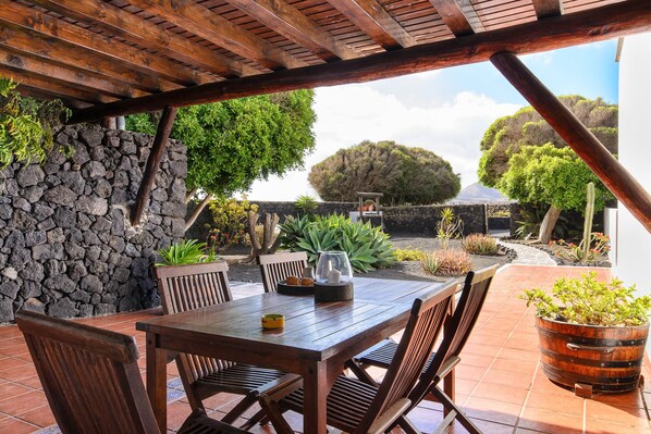 A wooden table with chairs, a stone wall, and potted plants.