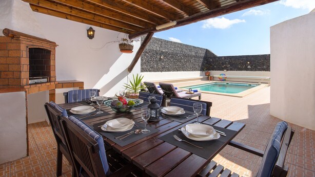 Ein Essbereich mit Backofen, Außenbestuhlung und Pool im Hintergrund.