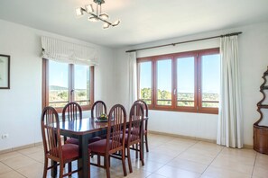 A dining area with a table and chairs, large windows with curtains, and a ceiling light fixture.