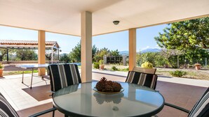 A covered outdoor dining area with a glass table, striped chairs, and a view of the surrounding landscape. - Rural Villa with pool and spectacular views – Villa Sastre (Campanet)
