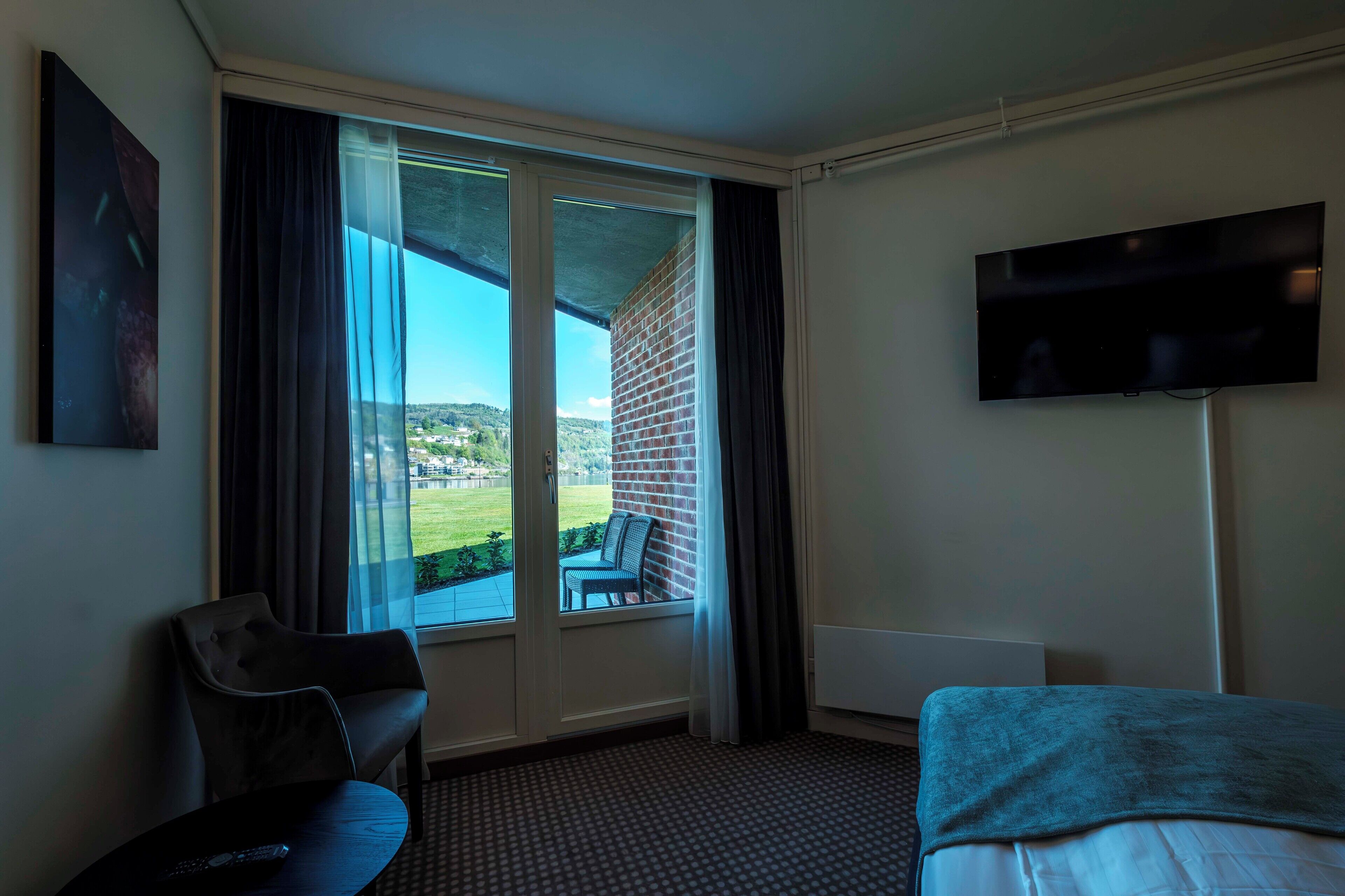 A hotel room with a large window, a flat-screen TV, a bed, and a chair.