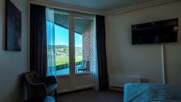 A hotel room with a large window, a flat-screen TV, a bed, and a chair.