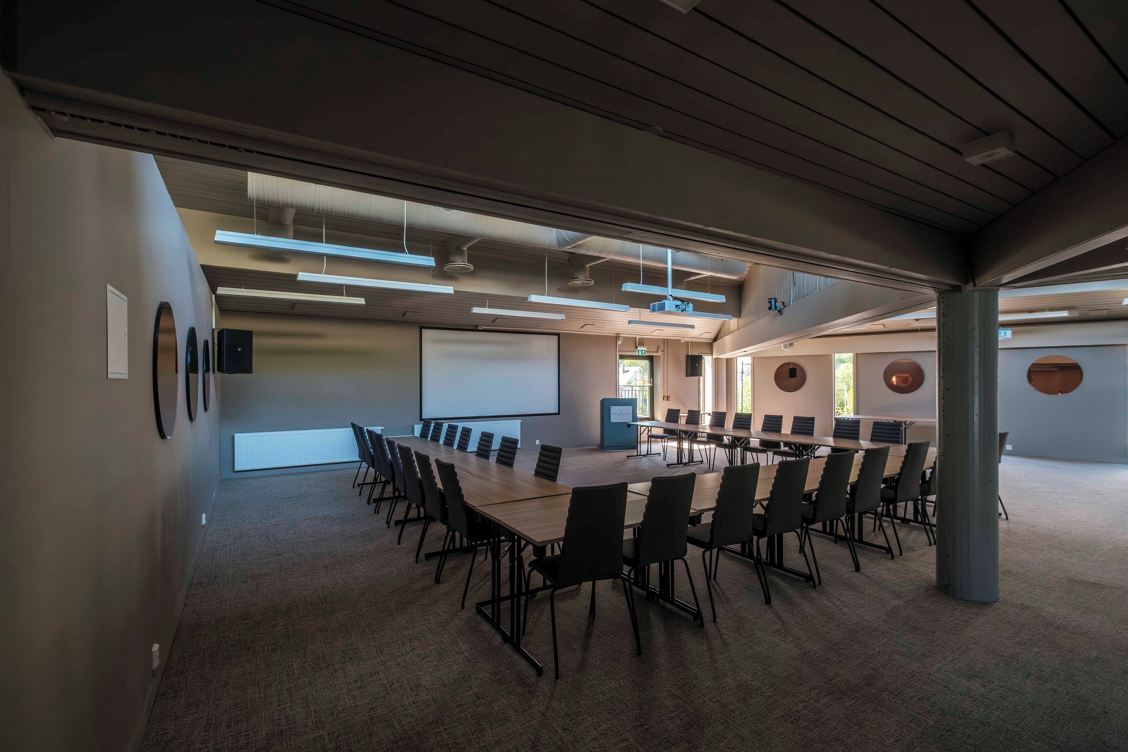 A conference room with a long table, multiple chairs, and a projector screen.