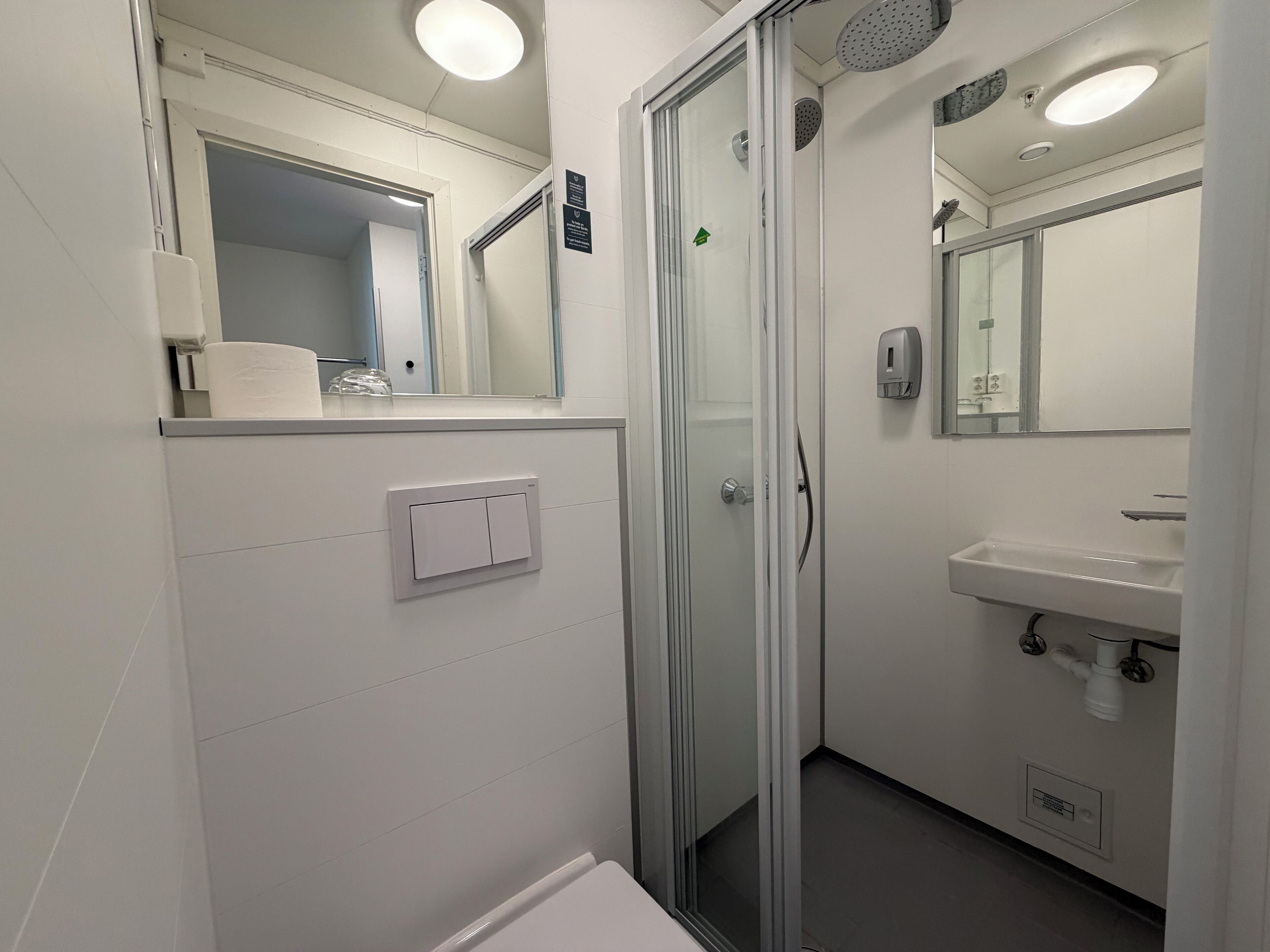 Un bagno moderno con cabina doccia in vetro, un lavandino bianco e uno specchio sopra il lavandino.