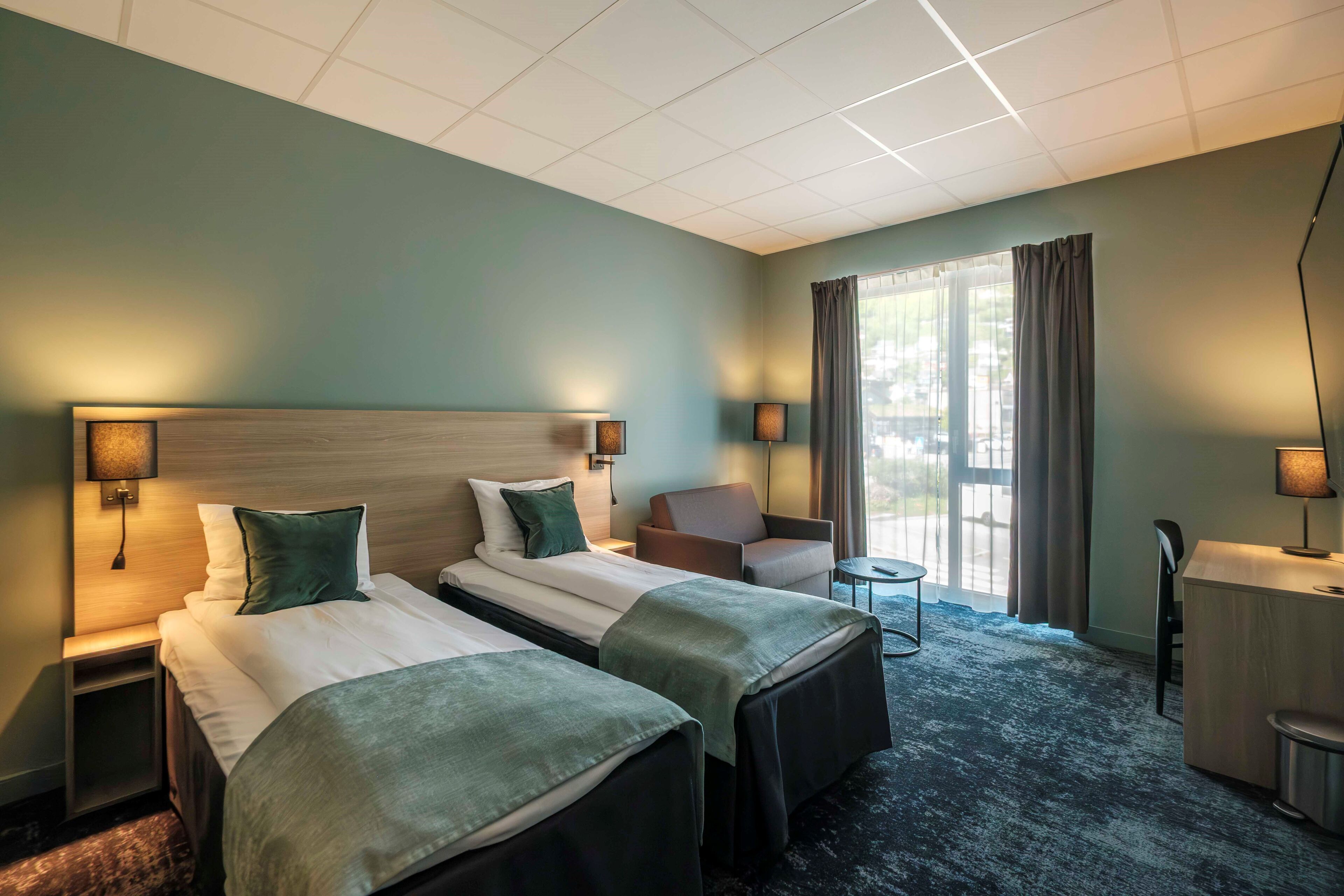 A hotel room with two beds, a desk, a chair, and a view of the outdoors.