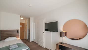 A hotel room with a bed, a desk, a TV, and a mirror.