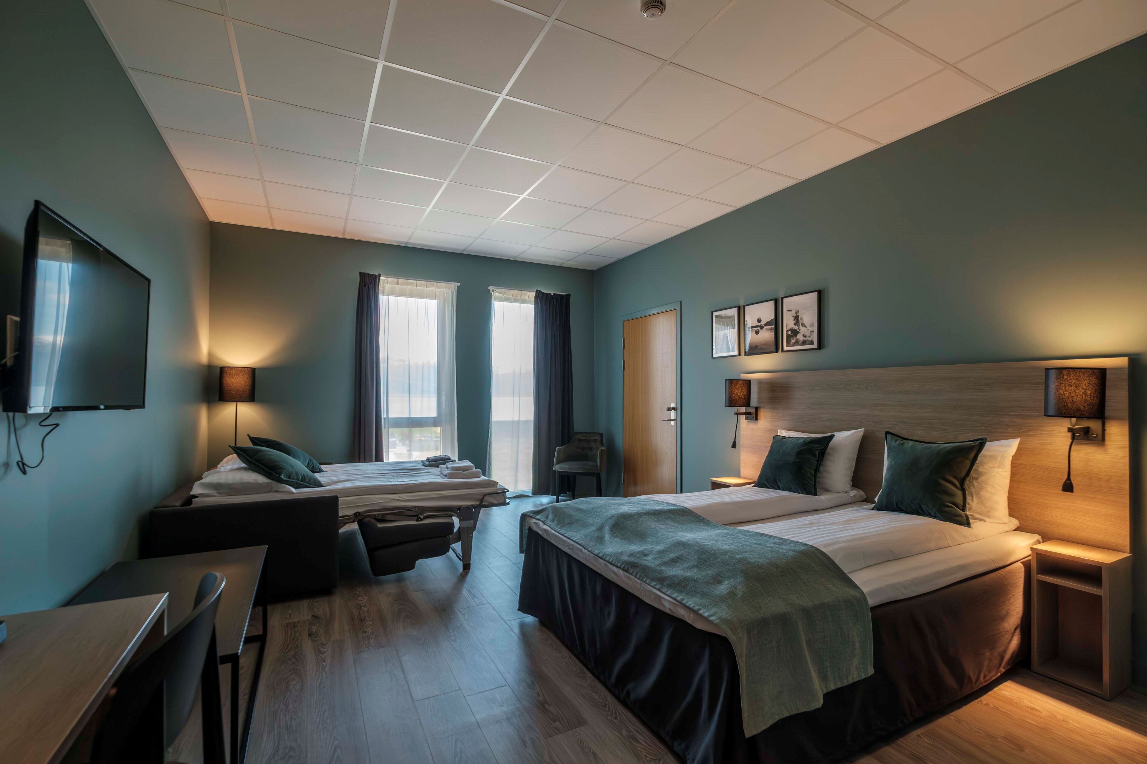 Habitación de hotel con dos camas, un escritorio, una silla, un televisor y una ventana con cortinas.