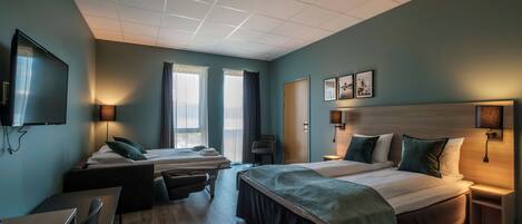 A hotel room with two beds, a desk, a chair, a TV, and a window with curtains.