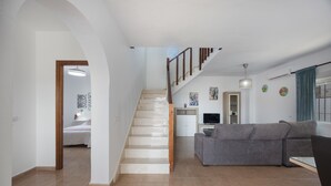 Uma sala de estar ampla com escada, um sofá cinza, uma televisão e uma mesa de jantar.
