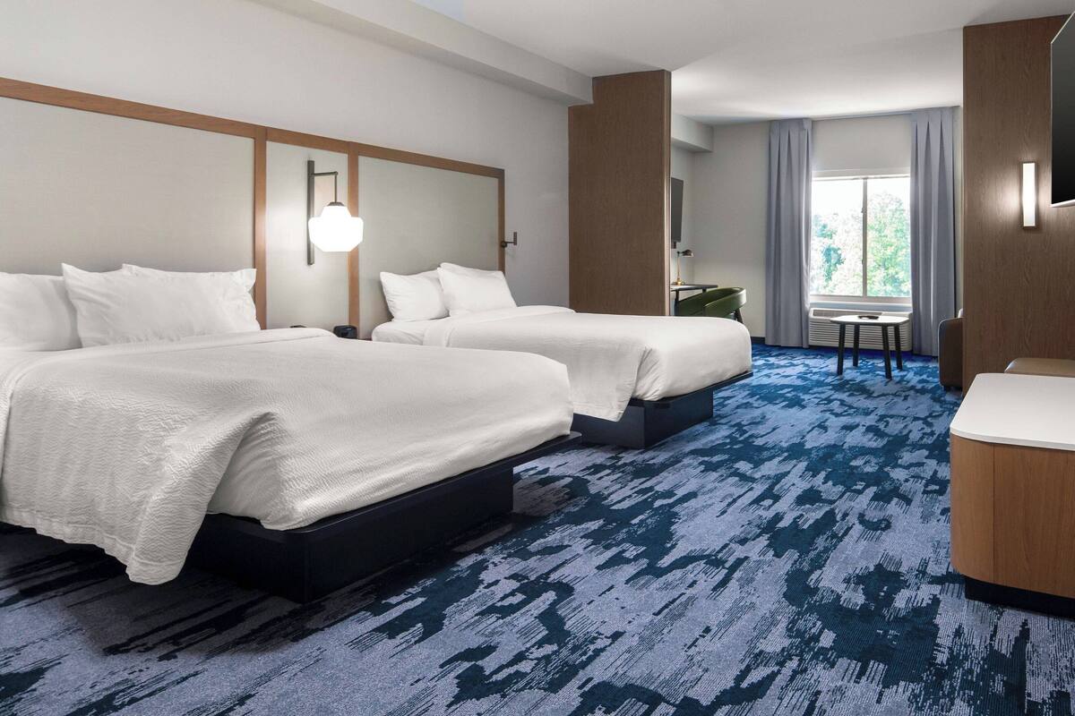 A hotel room with two beds, a small table, a TV, and a window with curtains.