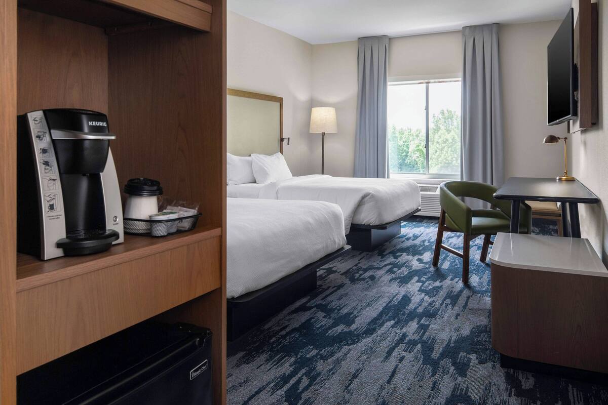 A hotel room with two beds, a desk, a chair, a coffee maker, and a TV.