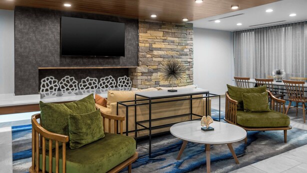 A modern living room with a stone accent wall, a flat-screen TV, a round coffee table, and two green upholstered chairs. - Fairfield Inn & Suites by Marriott Rocky Mount (Rocky Mount)