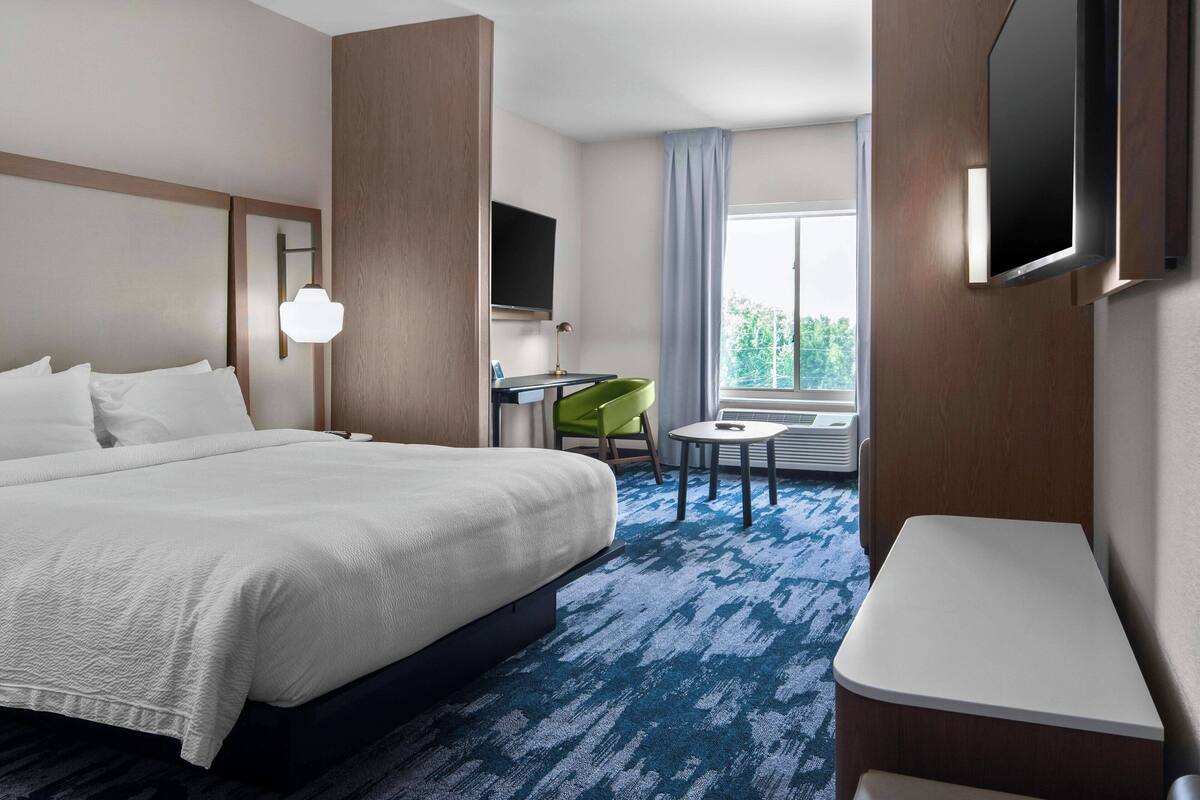 A hotel room with a large bed, a desk, a chair, a TV, and a window with a view.