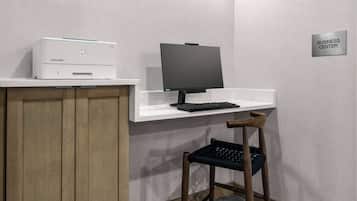 Un centro de negocios equipado con impresora, monitor, teclado y una silla.