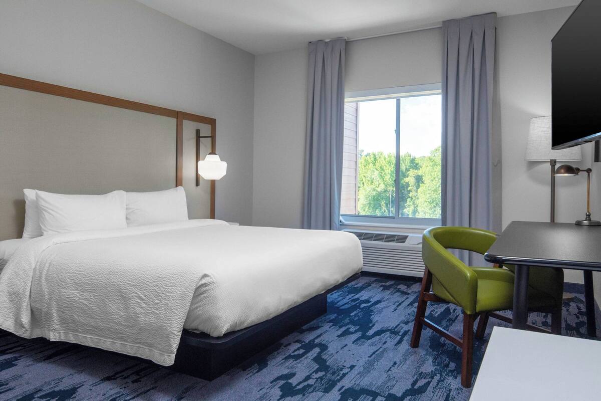 A hotel room with a large bed, a desk, a chair, a television, and a window with curtains.