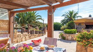 An outdoor patio with tables, chairs, and a stone wall. - Villa Smeralda 9 – Family Apartment with Pool near Olbia (Telti)