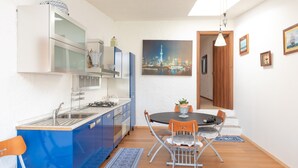 A compact kitchen with modern appliances, a dining area with a table and chairs, and a cityscape painting on the wall. - Villa Smeralda 9 – Family Apartment with Pool near Olbia (Telti)