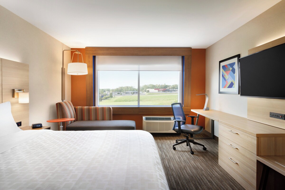 A hotel room with a bed, a desk, a chair, a sofa, a TV, and a window with a view of the outdoors.