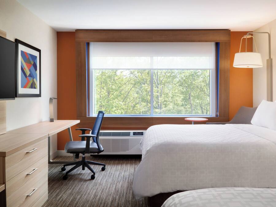 A hotel room with a bed, desk, chair, and a large window with a view of trees.