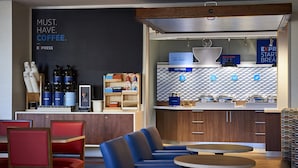 Un café moderno con un cartel de pizarra, zona de estar con sillas rojas y azules, y un salpicadero con diseño en el área de la cocina.