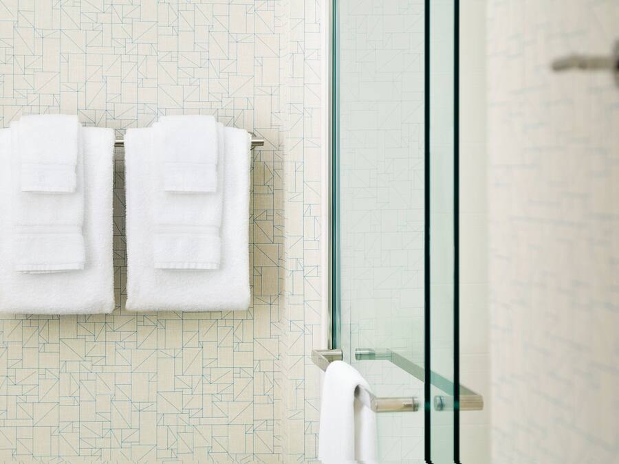 Ein Badezimmer mit Wand in geometrischem Muster, einer Duschkabine aus Glas und zwei weißen Handtüchern an einem Handtuchhalter.