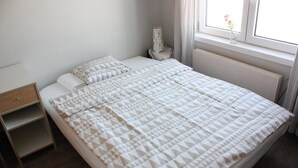 Uma cama bem arrumada com um edredom estampado com padrão geométrico, uma mesa de cabeceira com abajur e uma janela com cortinas.