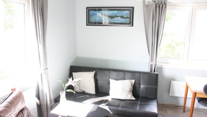 Uma sala de estar moderna com um sofá de couro preto, uma mesinha redonda e um quadro pendurado na parede.