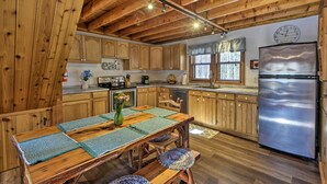 A rustic kitchen with wooden cabinets, a stainless steel refrigerator, and a dining table with green placemats. - Springwater Cabin Near Hiking, Lakes, & Vineyards (Springwater)