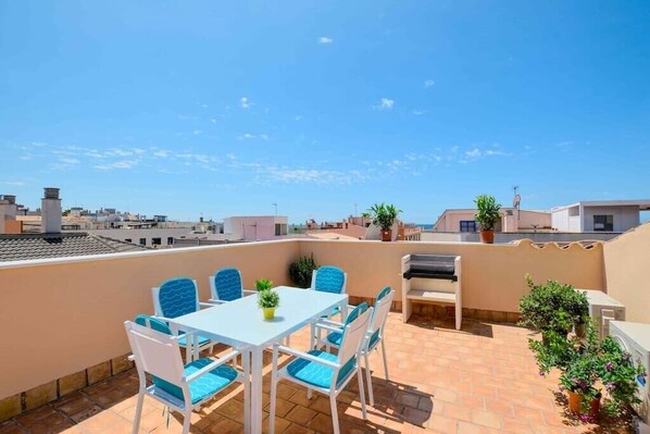Una terraza en la azotea con mesa y sillas, una parrilla y plantas en macetas.