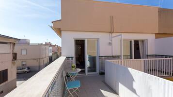 Un balcon avec une table et des chaises, une voiture garée devant, et un immeuble à la façade recouverte de carreaux.