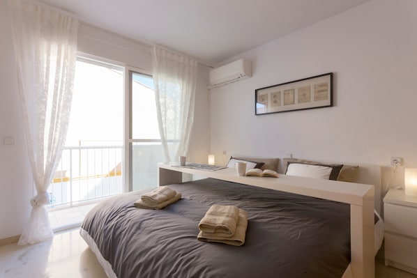 Ein Schlafzimmer mit Bett, Nachttischen, einem fensterbepflanzten Fenster und einer Wand-Klimaanlage.