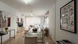 Un salon moderne avec une table à manger en verre, un canapé et une grande affiche illustrant l’alphabet, encadrée et accrochée au mur.