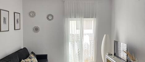 Una sala moderna con una mesa de comedor de vidrio, un sofá negro, un televisor sobre un mueble bajo y decoración en la pared.