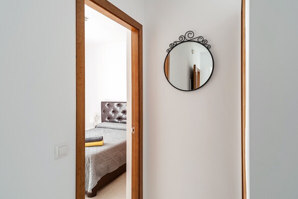 A bedroom with a bed, a round mirror, and a door leading to another room.