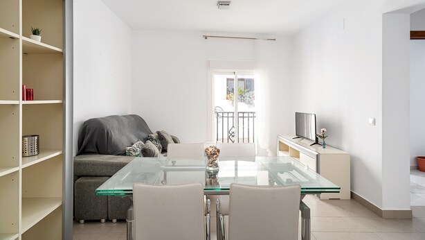 Una sala moderna con una mesa de vidrio, un sofá y un televisor sobre un mueble.