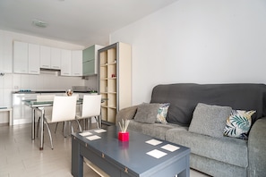Un espacio habitable moderno con comedor, kitchenette y un sofá gris con cojines decorativos.