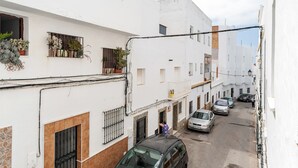 Una calle estrecha con edificios blancos, coches aparcados y una persona caminando.