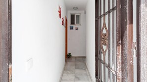Un pasillo estrecho con paredes blancas, piso de baldosas y una puerta con reja decorativa.